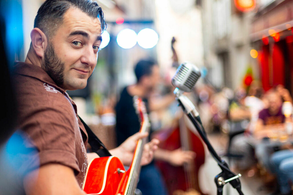 Musicien tenant une guitare et regardant le public devant un micro vintage lors d’un concert en terrasse chez Gourmet & Glouton à Chaudes-Aigues.