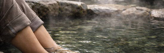 Personnes trempant les pieds dans une rivière alimentée par une source d’eau chaude, dans un environnement naturel et boisé