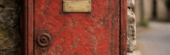 Ancienne boîte aux lettres rouge rouillée fixée sur un mur en pierre, symbole d’un espace de parole citoyenne locale