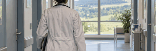 Femme médecin vue de dos avançant dans un couloir hospitalier.